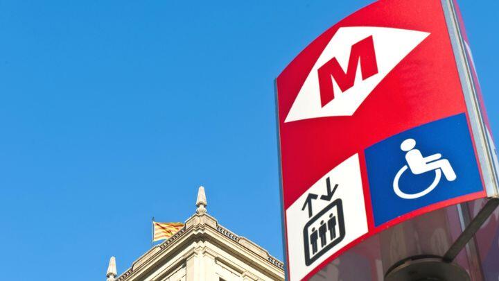 Red & white Barcelona Metro logo, plus disabled icon, on sign against blue sky