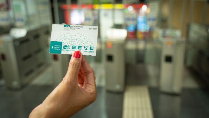 Close up of hand with red painted nails holding a BCN Barcelona public transport card, with metro turnstile in background