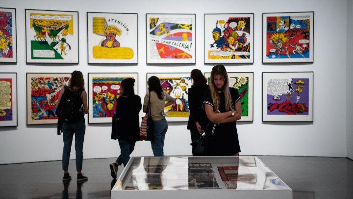 People browse in an art museum, against a wall hung with bright modern prints