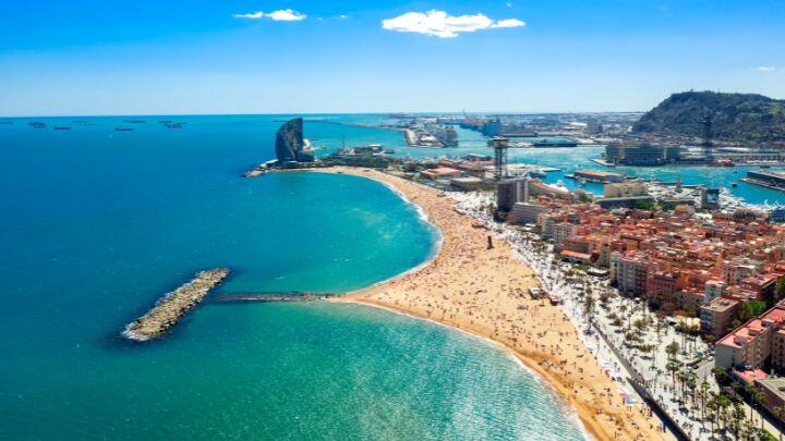 High aerial view of sandy Barceloneta beach, between blue/green sea to left and cityscape to right