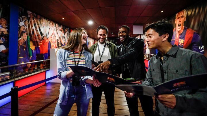 Group of young people look excitedly at brochures against display panels of footballers at Camp Nou museum