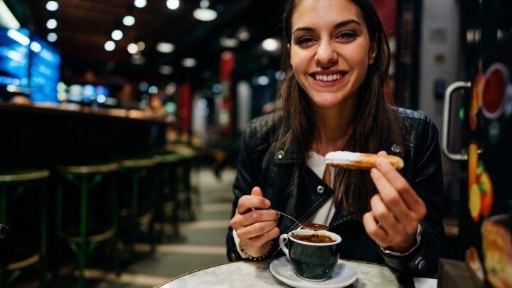 Woman enjoying churro and hot chocolate at café table in evening