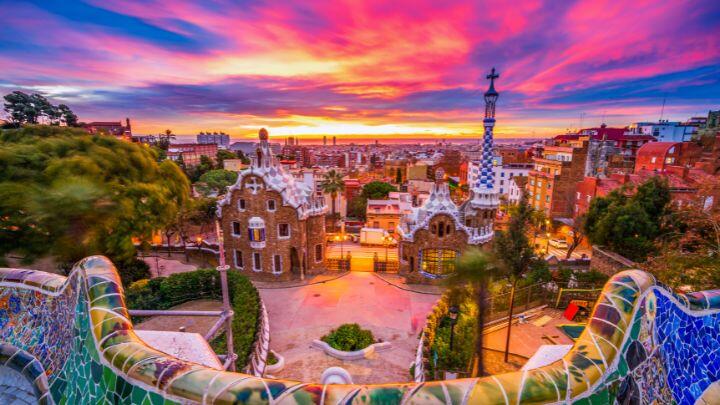 Sky streaked bright pink, orange and blue as sun sets over mosaic monuments at Parc Guell, Barcelona