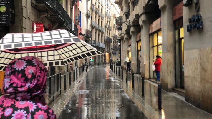 Cropped back view of woman in waterproof with umbrella looking along rainy street in Barcelona