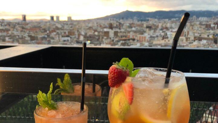 Close up of two cocktails with fruit and straws overlooking cityscape at sunset, Barcelona