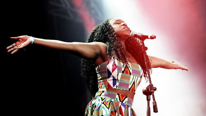 Singer in colourful dress spreads her arms at microphone