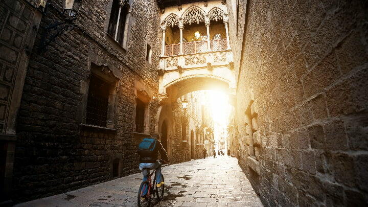 Cyclist passing beneath the iconic bridge between buildings in the Gothic Quarter