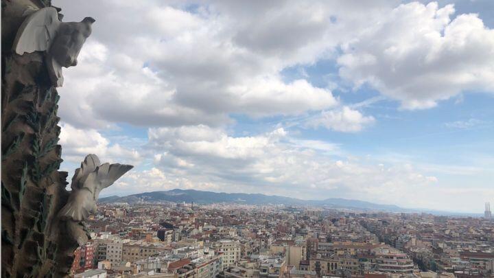 Close up of carved doves on tower of Sagrada Familia, overlooking cityscape and fluffy clouds