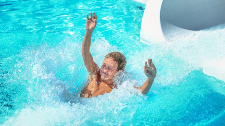Young boy splashes out of the end of a waterslide into turquoise pool water