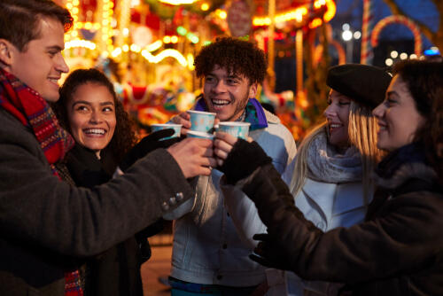 Friends share a drink at a christmas fair, with a carousel in the background