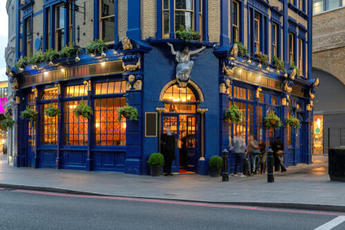 Front of a blue pub in London with lights on inside